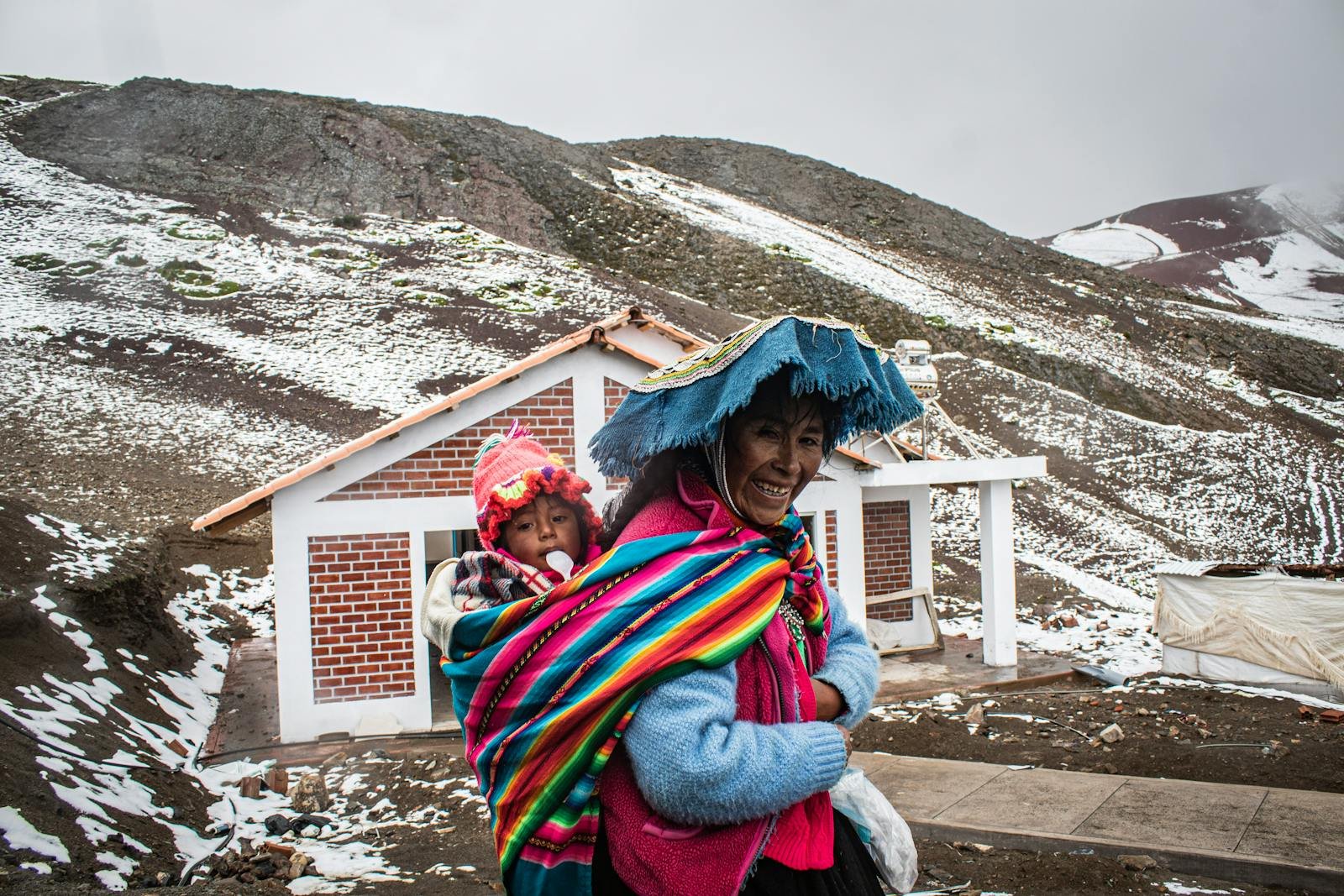 gente de los andes, Mother and child in colorful traditional attire in snowy Andean village setting.