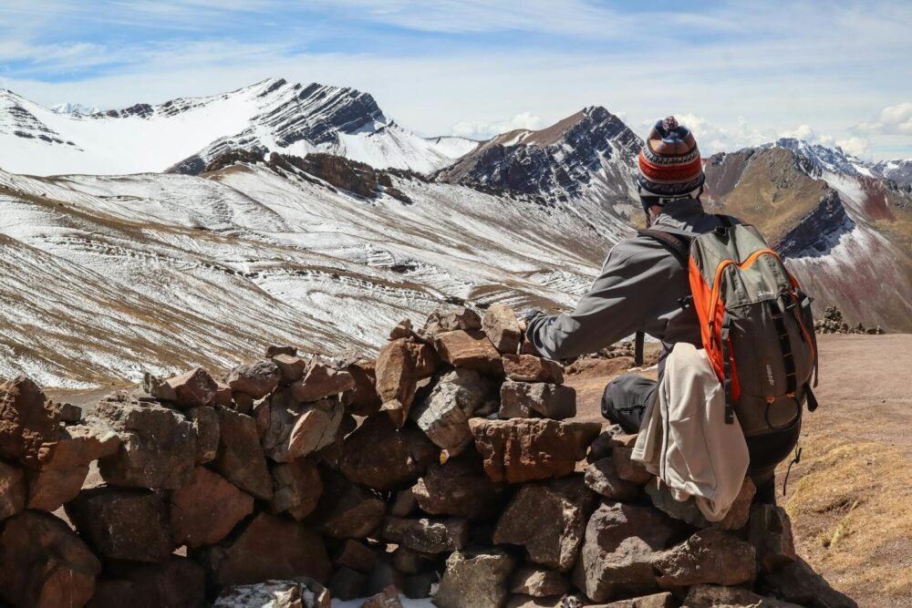 cooperación andinam A solo traveler rests by a stone wall, admiring the snow-covered Andes mountains.