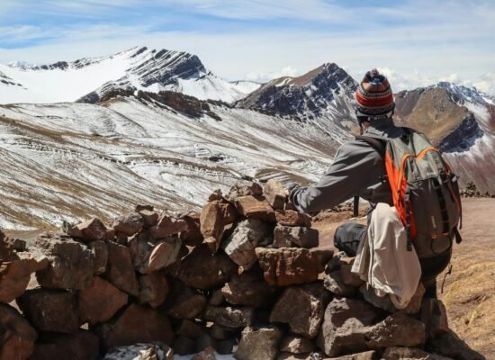 cooperación andinam A solo traveler rests by a stone wall, admiring the snow-covered Andes mountains.